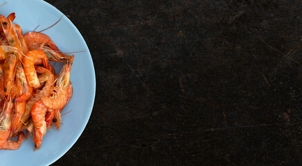 Shrimps on a blue plate on a dark background. Seafood. Shellfish. View from above. Place for text
