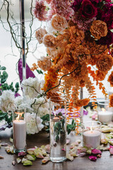 Candles, rose petals on floor. Closeup decor detail. Photo wall, arch decorated pink, orange flower for birthday party in banquet area, hall. Wedding reception for luxury ceremony. Decoration of event
