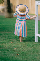 A little girl wearing a striped pastel dress holds a table leg while standing.