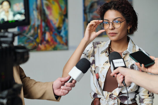 Young artist speaking to microphones, she giving an interview to journalists at art exhibition