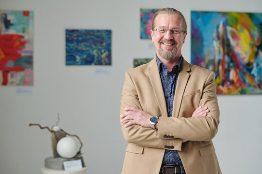 Portrait of mature owner of art gallery standing with his arms crossed and smiling at camera
