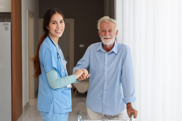Happy caregiver helping senior old man walking with walking frame stand up from bedroom at home or...