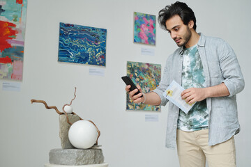 Young visitor making photo of modern art on his smartphone in art gallery