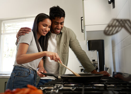 Happy young biracial couple in casual clothing cooking food in saucepan over stove in kitchen - Powered by Adobe