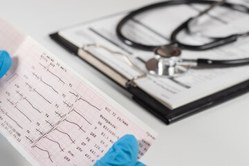 Doctor's hands hold result of the cardiogram next to patient sitting.