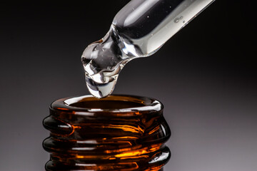 Stretched drop drips from the dropper into the bottle in the dark