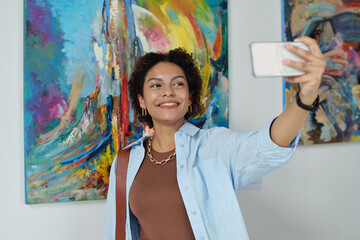 Smiling woman making selfie portrait on smartphone during her visit to art gallery