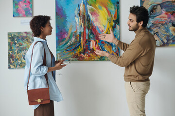 Young man discussing modern art with young woman during exhibition in gallery