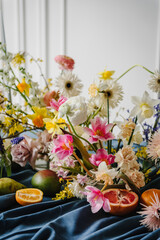 Festive decorated with flowers, fruits, greenery, candles. Beautiful bouquet in vase, orange, pear, pomelo, grapefruit on table. Home interior with decor elements. Summer composition of garden flowers
