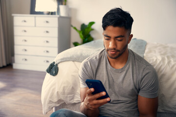 Young biracial man in casual clothing using mobile phone in bedroom at home