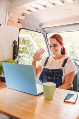 Young woman having a video call on the laptop inside her camper van. Van road trip holiday and outdoor summer adventure. Nomad lifestyle concept
