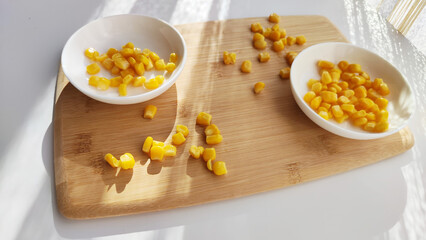 Lot of pieces of canned yellow corn on plate which is on wooden bamboo cutting board on white background. The concept of cooking and delicious healthy food