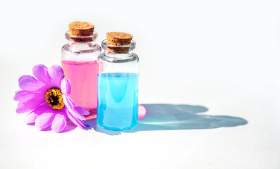 bottles of pink rose and blue essential oil transparent with a cork and with purple flower on a white background isolated, copy space for text. Spa beauty healthy lifestyle concept