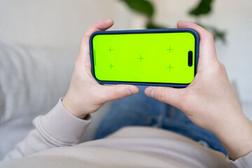 Man at home lying on a couch using smartphone with green mock-up screen. 