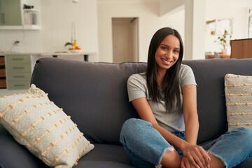 Happy young biracial woman in casual clothing sitting on sofa in living room at home - Powered by Adobe