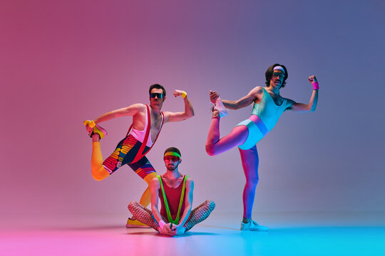 Funny, creative image of young men in stylish colorful sportswear training against gradient blue pink studio background in neon light. Concept of sportive and active lifestyle, humor, retro style. Ad