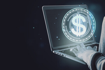 Close up of male hand holding and using laptop with digital round dollar sign on dark background with blurry mock up place. Online banking, cryptocurrency and finance concept.
