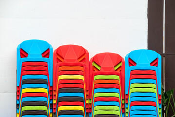 Stacks of multicolored plastic chairs against white wall in the street