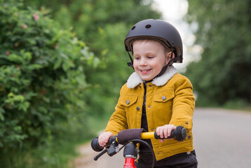Fototapeta na wymiar A cheerful little boy rides a running bike in a helmet outdoors. A happy child is engaged in an active sport. Protection. Life insurance and child safety.
