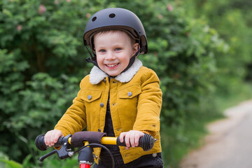 A cheerful little boy rides a running bike in a helmet outdoors. A happy child is engaged in an active sport. Protection. Life insurance and child safety.