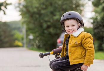 Fototapeta na wymiar A cheerful little boy rides a running bike in a helmet outdoors. A happy child is engaged in an active sport. Protection. Life insurance and child safety.