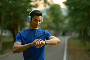 Sportsman wearing headphone checking his heart rate data on smartwatch during morning workout in the park