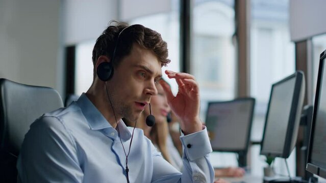 Nervous man talking headset in call center. Stressed support agent work hotline