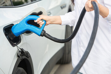 Young business woman refueling her electric car at a EV charging station. Concept of environmentally friendly vehicle. Electric car concept. Green travelling.