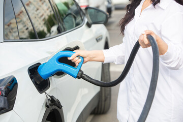 Young business woman refueling her electric car at a EV charging station. Concept of environmentally friendly vehicle. Electric car concept. Green travelling.