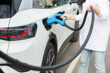 Young business woman refueling her electric car at a EV charging station. Concept of environmentally friendly vehicle. Electric car concept. Green travelling.