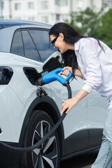 Plakat Young business woman refueling her electric car at a EV charging station. Concept of environmentally friendly vehicle. Electric car concept. Green travelling.