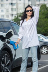 Young business woman refueling her electric car at a EV charging station. Concept of environmentally friendly vehicle. Electric car concept. Green travelling.