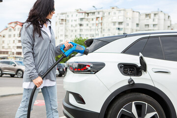 Young business woman refueling her electric car at a EV charging station. Concept of...