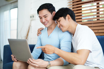 Obraz premium Gay Couple Using Computer For Video Conference On Sofa. Diversity of LGBTQ relationships. A gay couple living together concept