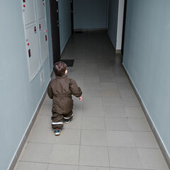 A child walks down the corridor of an apartment building. Baby comes out of the apartment door for a walk into the dark corridor of the house. Kid aged about two years (one year ten months)