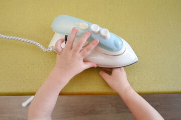 The child's careless behavior in playing with a hot iron in the living room could result in burns or injuries to the baby if left unsupervised. Kid aged about two years (one year ten months)