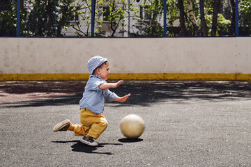 A child falls while playing with a ball on a football field. Kid aged about two years (one year...