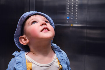 Happy baby rides in the elevator of an apartment building with buttons on the wall. A child in an elevator with metal walls. Kid aged about two years (one year eleven months)