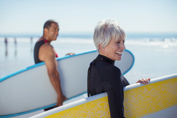 Senior couple carrying surfboards on beach