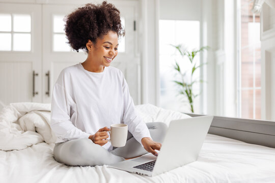 happy young african american woman relaxing with laptop at home lying in bed  .