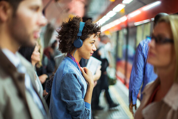 Woman listening to headphones in train station - obrazy, fototapety, plakaty