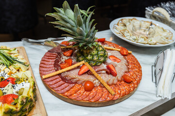 Selection of smoked sausage, winter sausage, prosciutto, decorated with fruit, on plate.