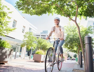 Tuinposter Smiling young woman with helmet riding bicycle in urban park © KOTO