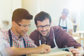 Smiling carpenters measuring wood with ruler in workshop