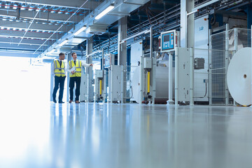 Workers walking along machinery in factory