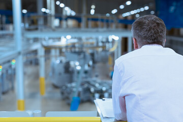 Supervisor with clipboard on platform overlooking factory