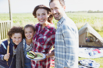 Portrait smiling family with barbecued hamburgers at sunny campsite