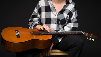 The girl holds a guitar on her knees and plays with one hand