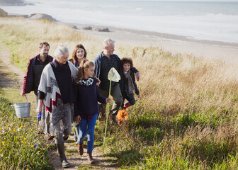 Multi-generation family walking nets bucket on sunny grass beach path - obrazy, fototapety, plakaty