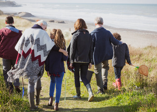Multi-generation family walking on sunny grass beach path